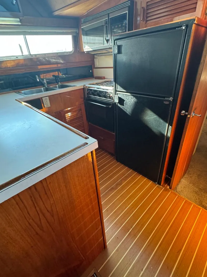 Slide: The Image of 1984 Tollycraft 48 Cockpit Motor Yacht kitchen with wood flooring and black appliances. - 37