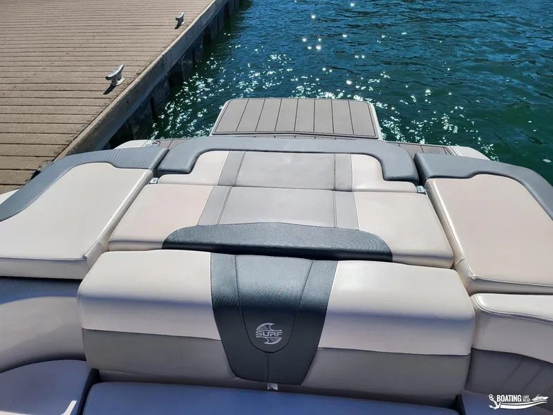 Slide: The Image of 2021 Chaparral 23 Surf boat at dock, featuring cushioned seating and sunlit water. - 11