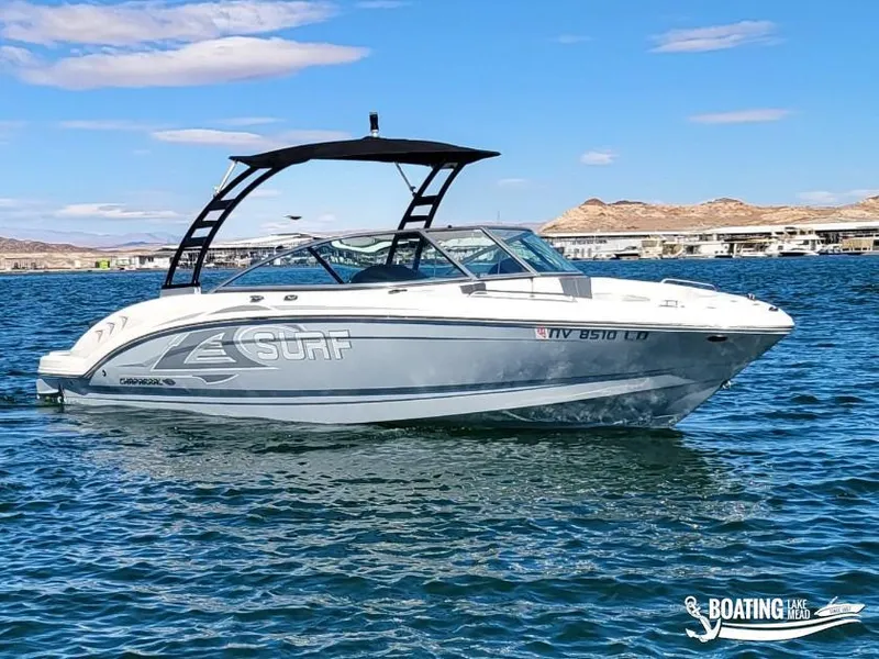 Slide: The Image of 2021 Chaparral 23 Surf boat on a lake with clear skies and distant hills. - 2