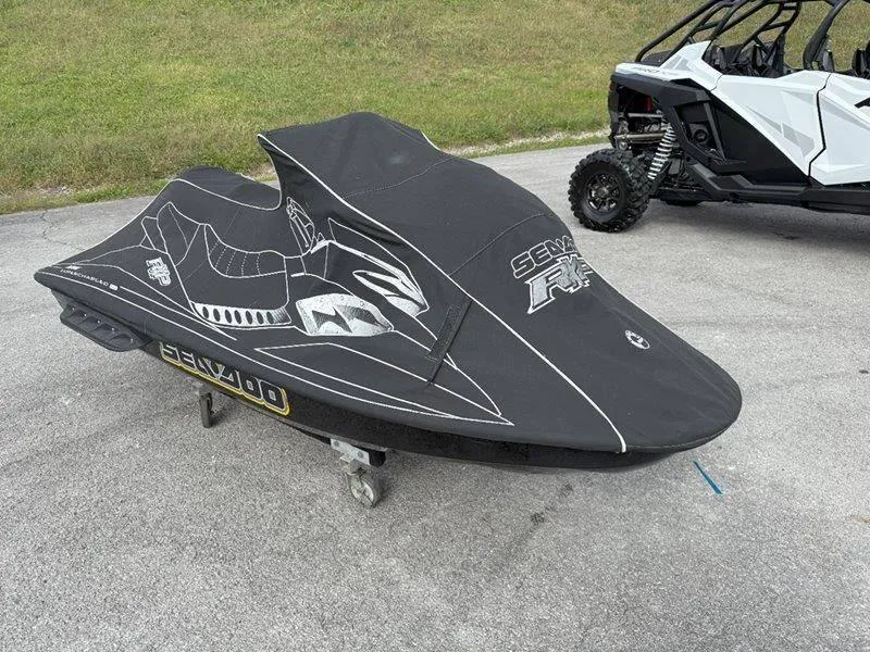 Slide: The Image of 2007 Sea-Doo RXP 215 jet ski covered, parked on pavement near off-road vehicle. - 12