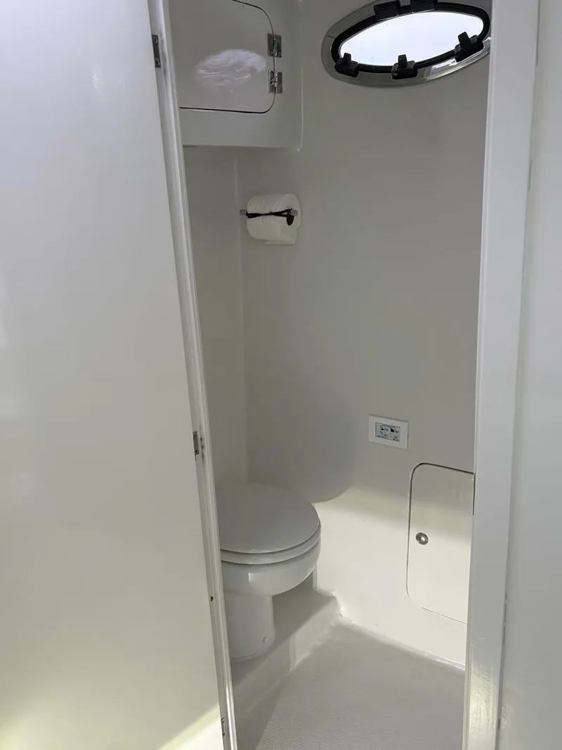 Slide: The Image of 2023 Millennium Marine NuWave Walkaround boat interior bathroom with toilet and porthole. - 11