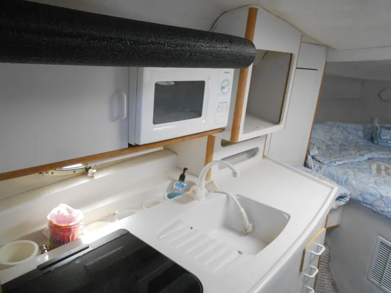 Slide: The Image of 1995 Larson 280 Cabrio interior with kitchenette, microwave, sink, and cozy sleeping area. - 14