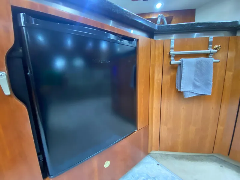 Slide: The Image of 2006 Cruisers Yachts 52 Express kitchen with black fridge and wooden cabinetry. - 54