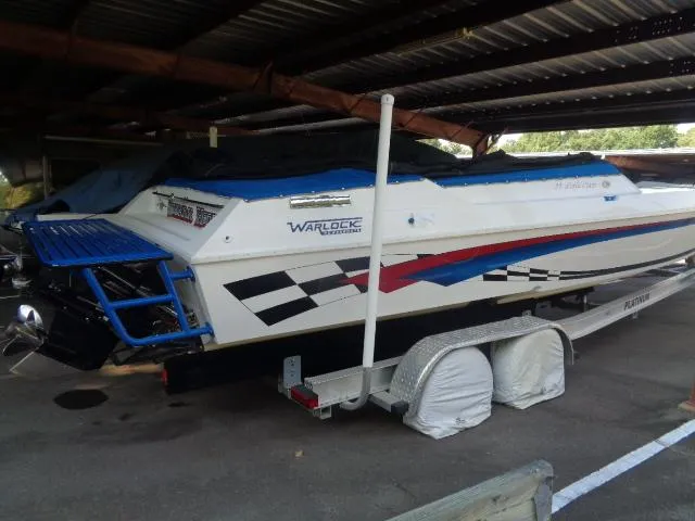 Slide: The Image of 2001 Warlock 29 World Class boat in storage, featuring vibrant graphics and covered trailer. - 16