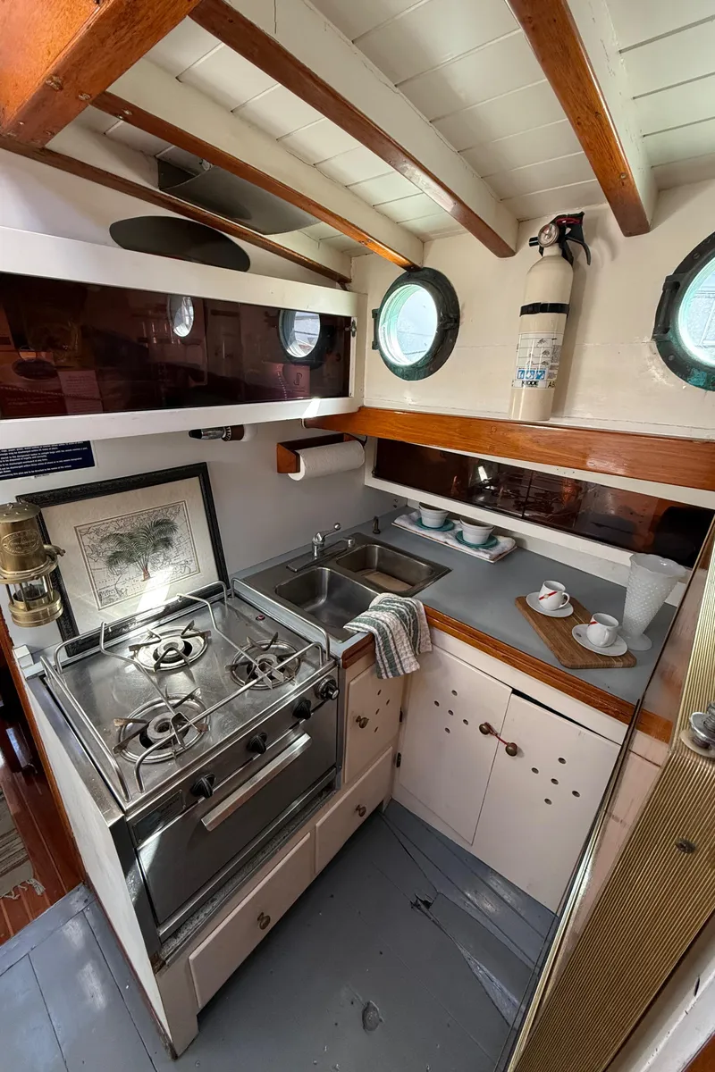 Slide: The Image of Interior of 1932 Historic Fellows & Stewart Yawl, featuring a compact kitchen with stove and sink. - 25