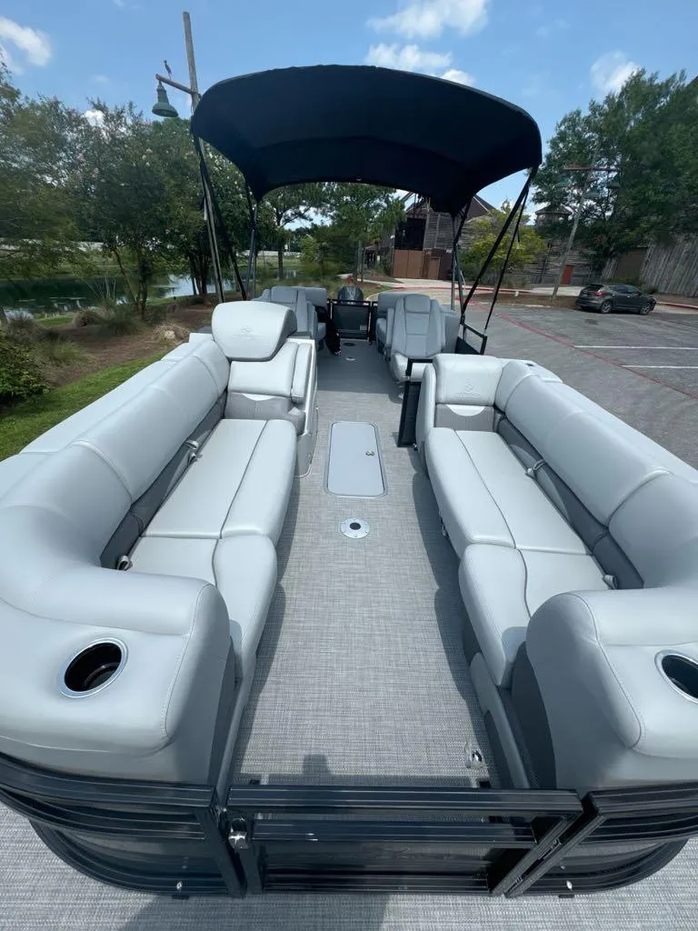 Slide: The Image of 2025 Regency 230 DL3 pontoon boat with spacious seating and canopy, parked outdoors. - 4