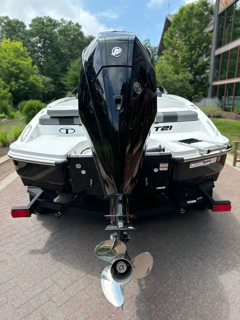 Slide: The Image of 2025 Tahoe T21 boat on trailer, parked on a brick pathway, surrounded by greenery. - 2