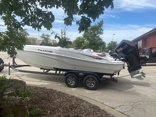 Slide: The Image of 2025 Tahoe T21 boat on trailer, parked outdoors under a tree. - 2