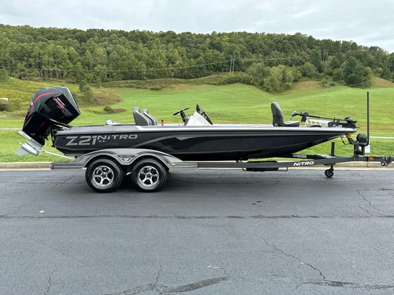 The Image of 2025 Nitro Z21 XL boat on trailer, parked on asphalt with green hills in background. - 0