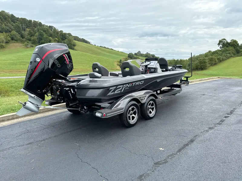 Slide: The Image of 2025 Nitro Z21 XL boat on trailer, parked on asphalt near grassy hills. - 2