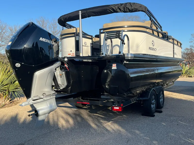 Slide: The Image of 2025 Regency 230 DL3 pontoon boat with Mercury outboard motor, parked on a trailer. - 2