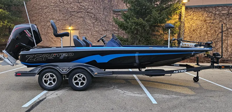 The Image of 2025 Nitro Z21 XL boat on trailer, sleek black and blue design, parked outdoors. - 0