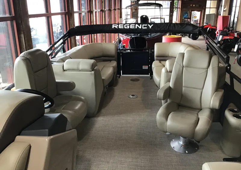 Slide: The Image of 2025 Regency 230 DL3 pontoon boat interior with beige seating and spacious layout. - 2