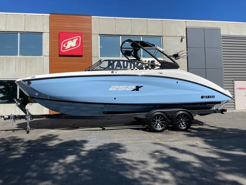 Slide: The Image of 2024 Yamaha Boats 252XE in blue, parked on a trailer outside a building. - 0