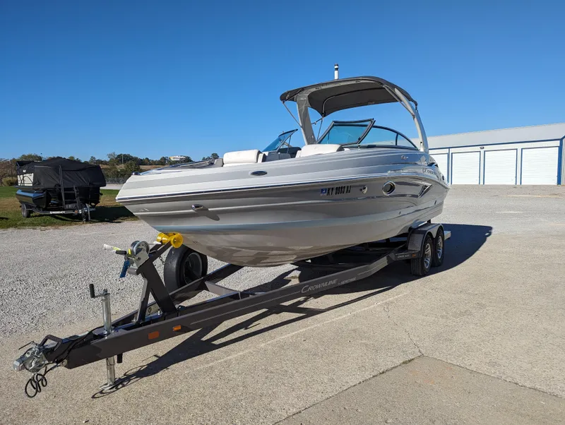 Slide: The Image of 2023 Crownline 260 SS boat on trailer, parked outdoors under clear blue sky. - 14
