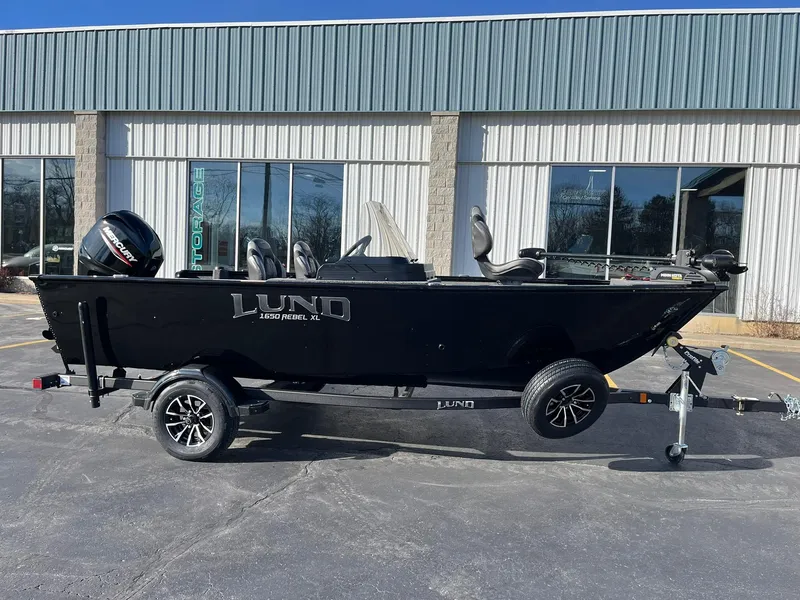 Slide: The Image of 2025 Lund 1650 Rebel XL SS boat on trailer, parked outside a building. - 2