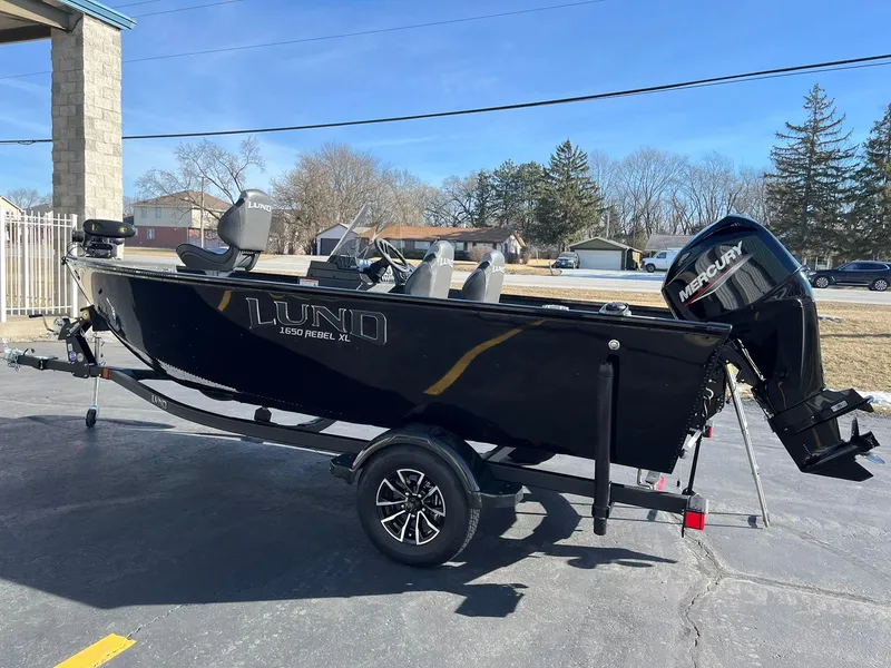 Slide: The Image of 2025 Lund 1650 Rebel XL SS boat on trailer, parked outdoors, featuring Mercury outboard motor. - 3