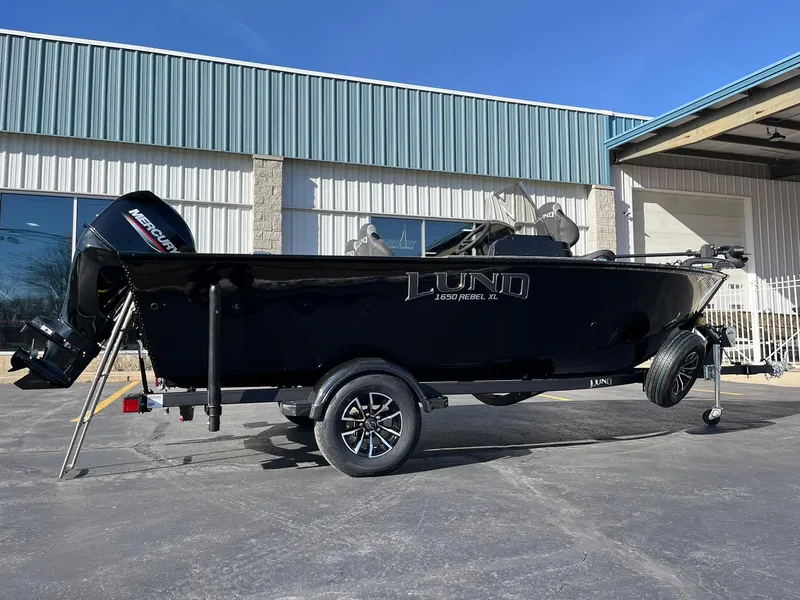 Slide: The Image of 2025 Lund 1650 Rebel XL SS boat on trailer, parked outside a building. - 4