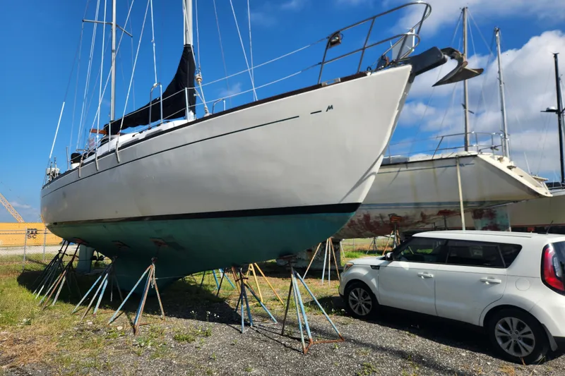 Slide: The Image of 1979 Morgan 45 Ketch sailboat on stands beside a white car, under a clear blue sky. - 5
