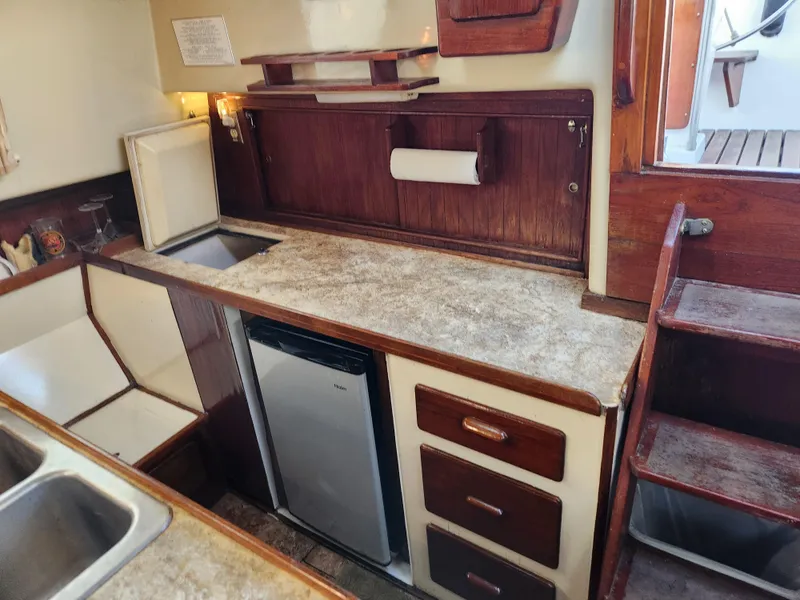 Slide: The Image of 1979 Morgan 45 Ketch kitchen with wooden cabinetry, compact fridge, and countertop. - 50