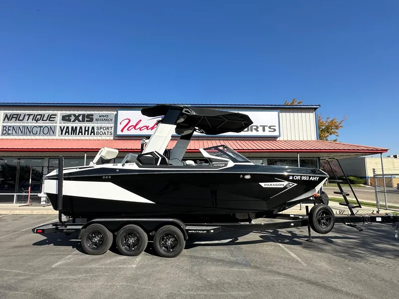 Slide: The Image of 2023 Nautique PARAGON 23 boat on trailer outside dealership under clear blue sky. - 2