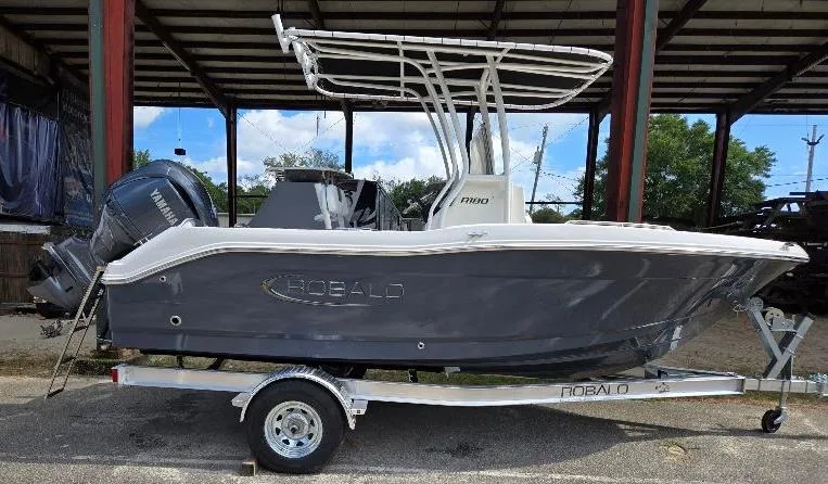 The Image of 2025 Robalo R180 Center Console boat on trailer, parked under a shelter. - 0