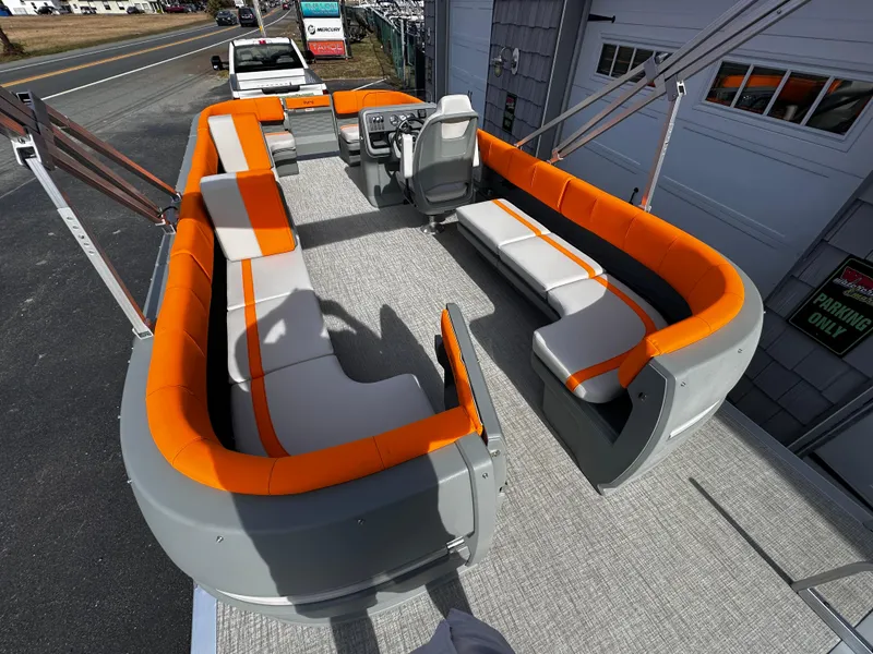 Slide: The Image of 2025 Avalon 2385 Aura Quad Lounge boat with orange and gray seating, docked near a garage. - 10