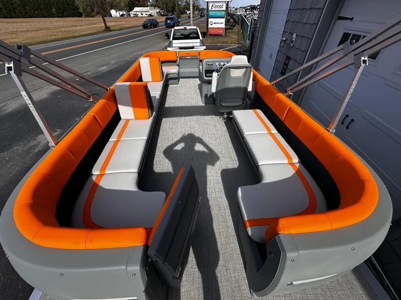 Slide: The Image of 2025 Avalon 2385 Aura Quad Lounge pontoon boat with orange and gray seating, parked outdoors. - 11