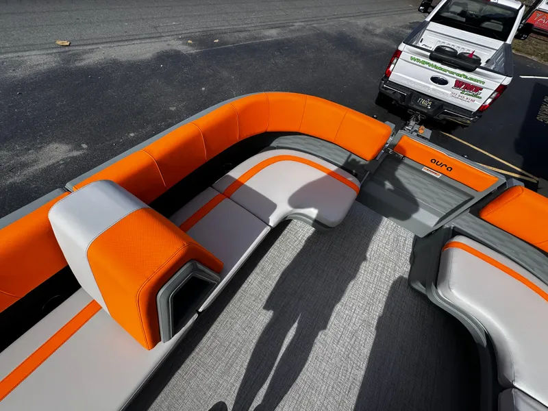 Slide: The Image of 2025 Avalon 2385 Aura Quad Lounge boat with orange and gray seating, parked near a truck. - 14