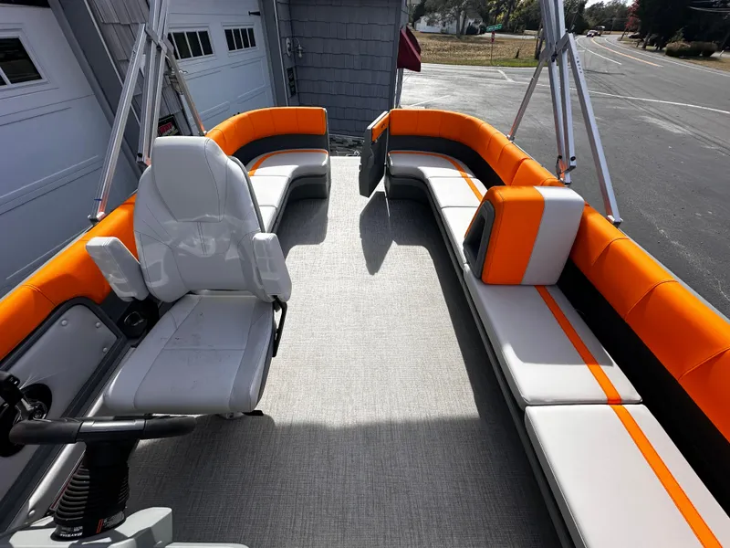 Slide: The Image of 2025 Avalon 2385 Aura Quad Lounge boat with orange and white seating, docked outdoors. - 15