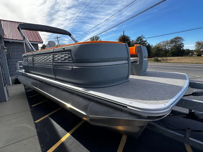 Slide: The Image of 2025 Avalon 2385 Aura Quad Lounge pontoon boat, gray and orange, parked outdoors. - 6