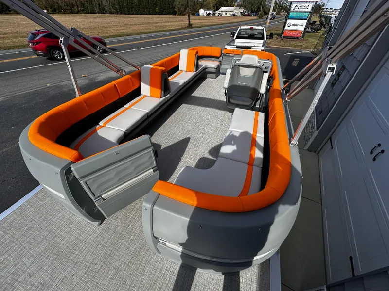 Slide: The Image of 2025 Avalon 2385 Aura Quad Lounge boat with orange and gray seating, parked on a road. - 9