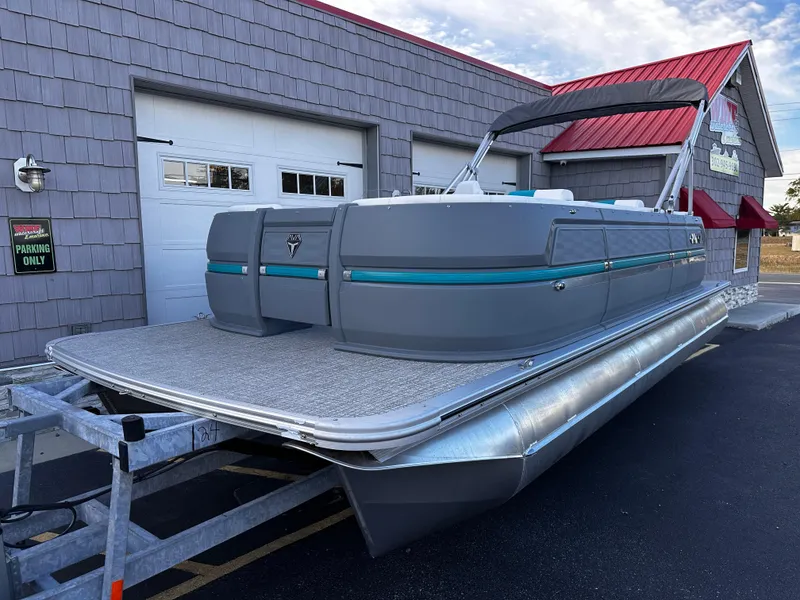 Slide: The Image of 2025 Avalon 2385 Aura Quad Lounge pontoon boat on trailer, parked outside a building. - 2