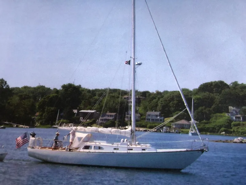 Slide: The Image of 1968 LeComte Northeast 38 sailboat on calm water, with lush green shoreline in the background. - 1