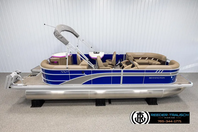 The Image of 2025 Bennington 23 SXPDSE pontoon boat with blue exterior and tan seating, displayed indoors. - 1