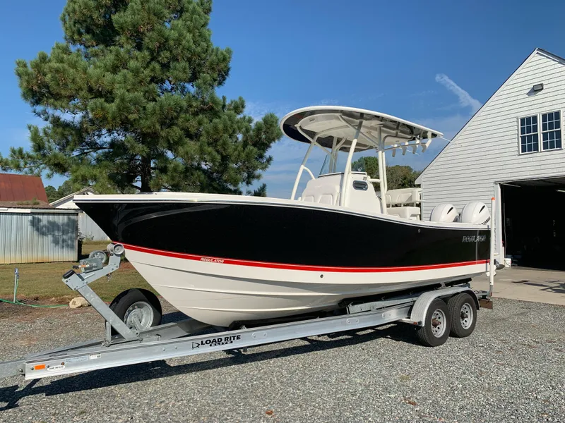 Slide: The Image of 2019 Regulator 23 FS boat on trailer, parked near a white building. - 2
