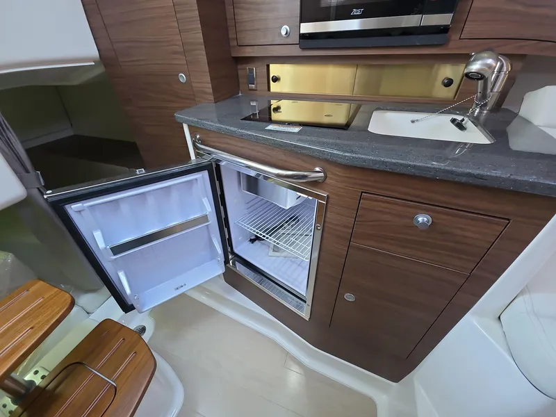 Slide: The Image of 2025 Boston Whaler 325 Conquest interior kitchen with open fridge and modern wood cabinetry. - 12