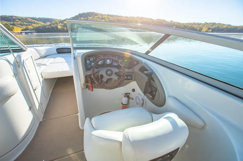 Slide: The Image of 2006 Crownline 270 BR boat interior with steering wheel and seating, on a sunny lake. - 16