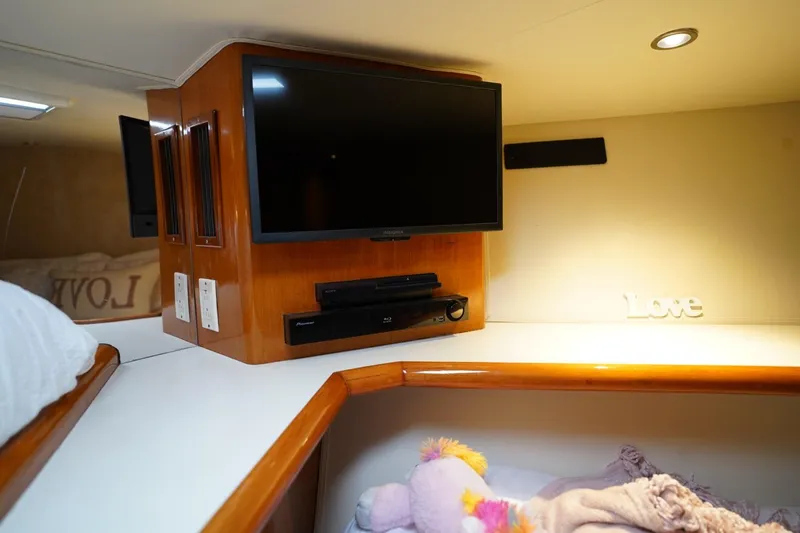 Slide: The Image of 1999 Viking 55 Convertible yacht interior with TV, wooden cabinetry, and cozy bedding. - 49