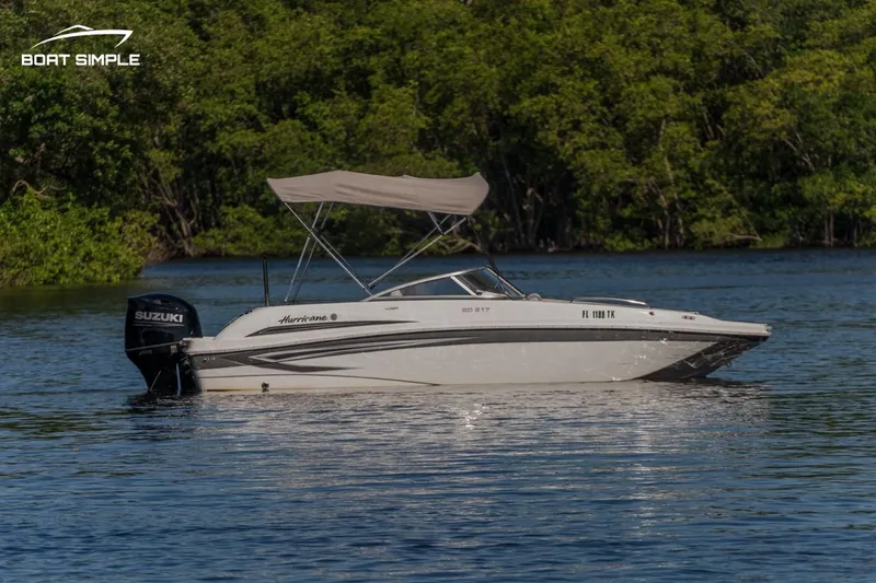 Slide: The Image of 2022 Hurricane SunDeck 217 OB boat on calm water, surrounded by lush greenery. - 0