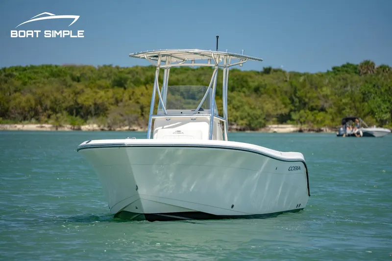 Slide: The Image of 2021 Cobia 201 Center Console boat on calm water, with lush green shoreline. - 1