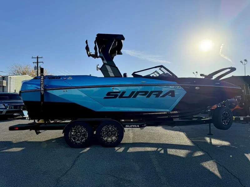 Slide: The Image of 2025 Supra SA boat on trailer, blue and black design, parked outdoors in sunlight. - 5