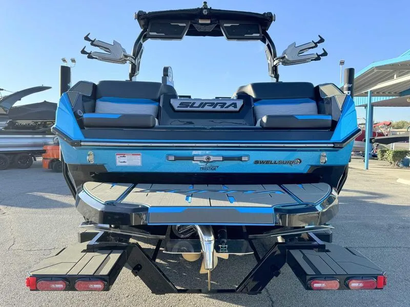 Slide: The Image of 2025 Supra SA boat rear view, blue and black design, parked outdoors. - 7