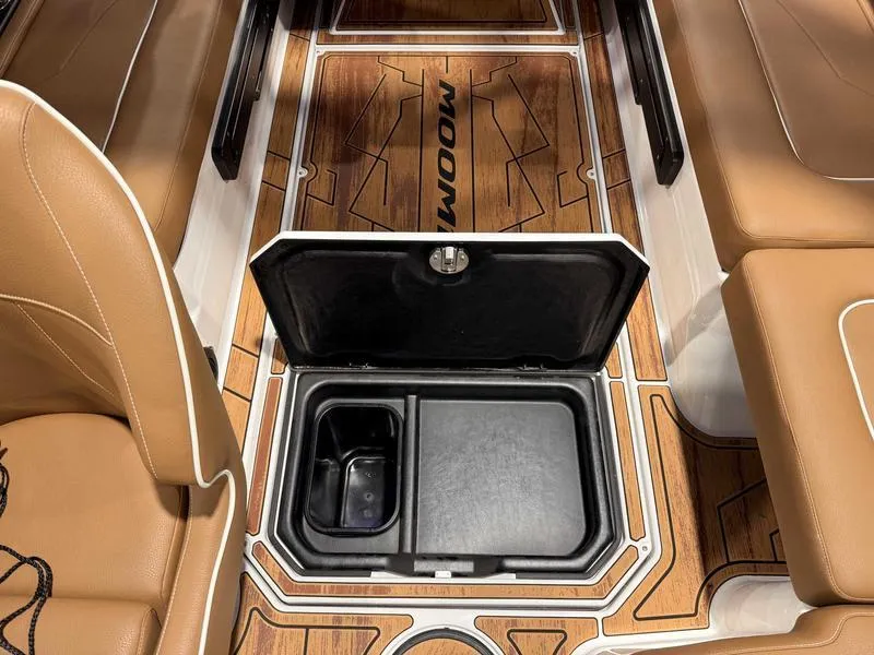 Slide: The Image of 2025 Moomba Mojo boat interior with open storage compartment, brown seating, and wood-patterned flooring. - 10