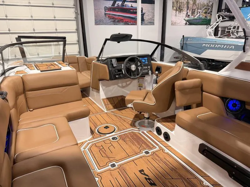 Slide: The Image of 2025 Moomba Mojo boat interior with tan seating and modern dashboard in a showroom. - 5
