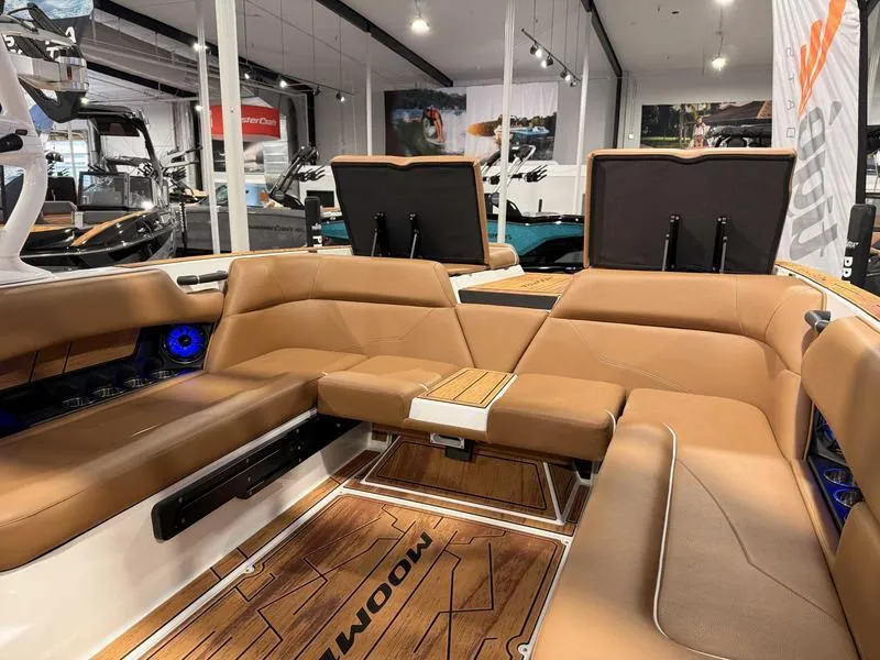 Slide: The Image of 2025 Moomba Mojo boat interior with tan seating and wood accents in showroom. - 9