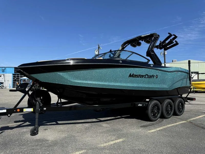 Slide: The Image of 2025 MasterCraft X24 boat on trailer, parked outdoors under clear blue sky. - 2