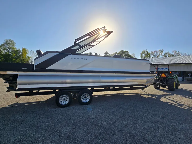 Slide: The Image of 2025 Manitou 240 Cruise pontoon boat on trailer, sunlit background. - 3