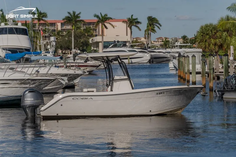 Slide: The Image of 2023 Cobia 220 Center Console boat docked in a marina with palm trees. - 1