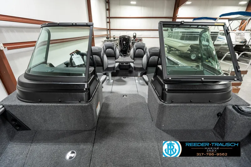 Slide: The Image of 2025 Lund 1775 Impact XS boat interior in showroom, featuring dual consoles and seating. - 13